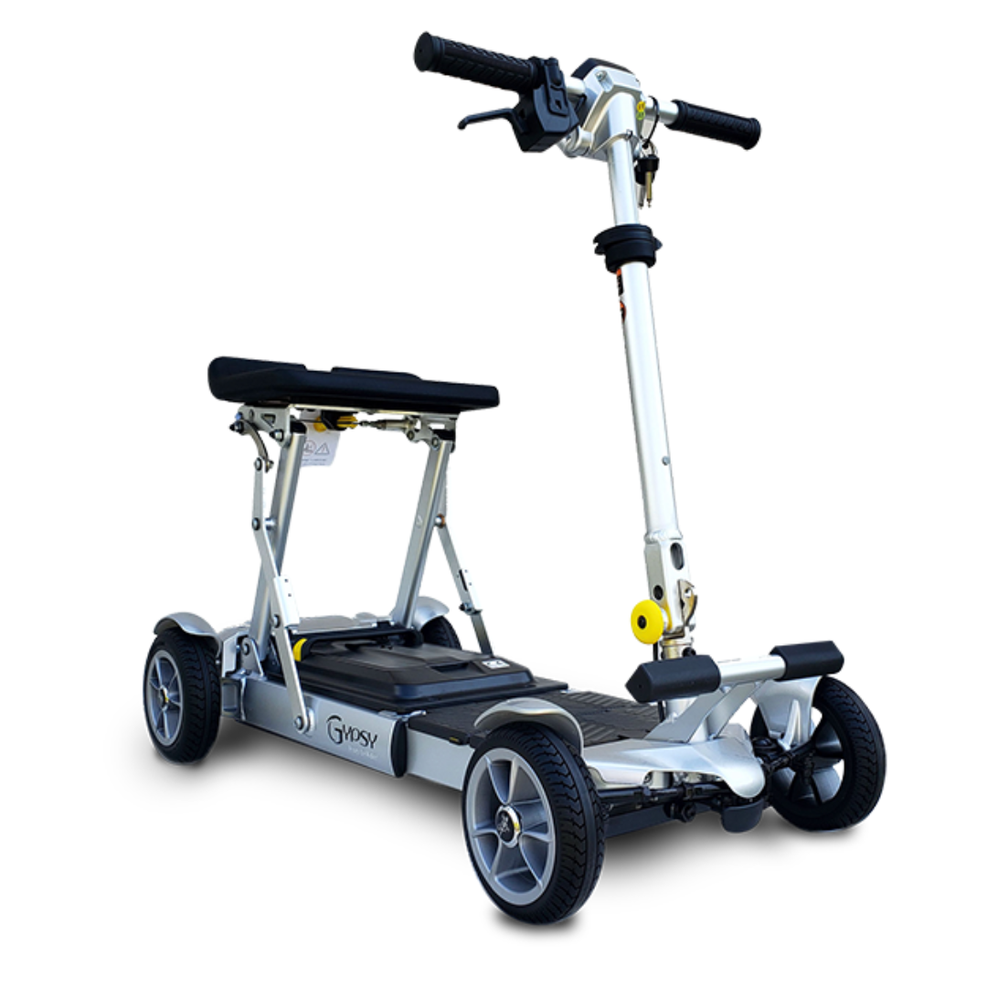 The EV Rider Gypsy Ultra Compact Airline Approved Scooter is a silver, four-wheeled folding mobility scooter with a foldable seat and handlebars, black platform, and sturdy frame, designed for personal mobility and outdoor use, shown on a white background.